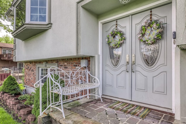 view of exterior entry with stucco siding, brick siding, and fence