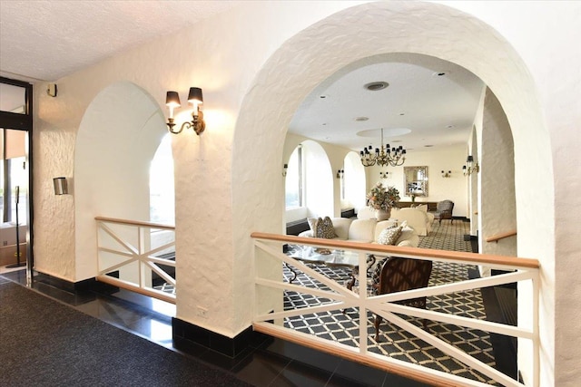 hallway featuring arched walkways, a textured wall, and a notable chandelier
