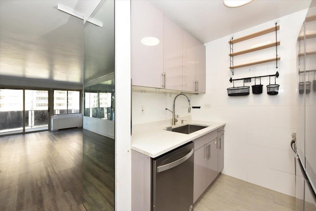 kitchen featuring a sink, light countertops, open floor plan, wood finished floors, and stainless steel dishwasher