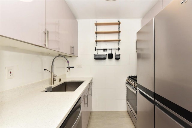 kitchen featuring tile walls, appliances with stainless steel finishes, a sink, and light stone counters