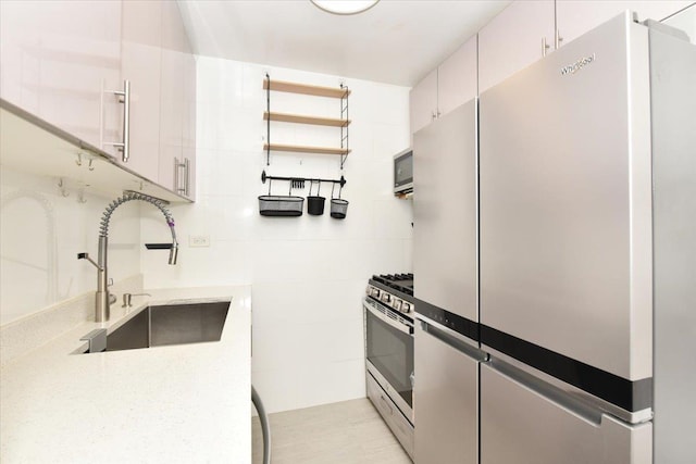 kitchen with open shelves, light stone counters, a sink, stainless steel appliances, and white cabinetry