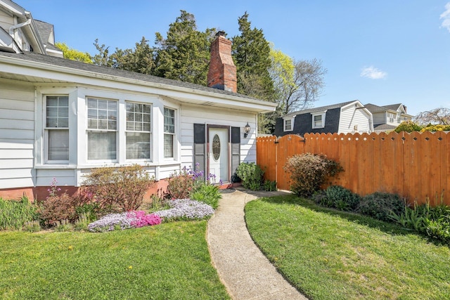 entrance to property with a lawn, fence, and a chimney