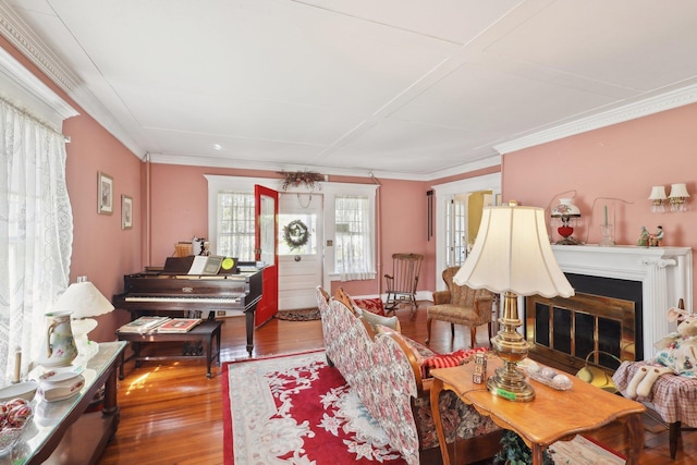 living area with a glass covered fireplace, ornamental molding, and wood finished floors
