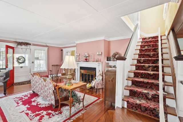 living room with ornamental molding, a glass covered fireplace, wood finished floors, and stairway