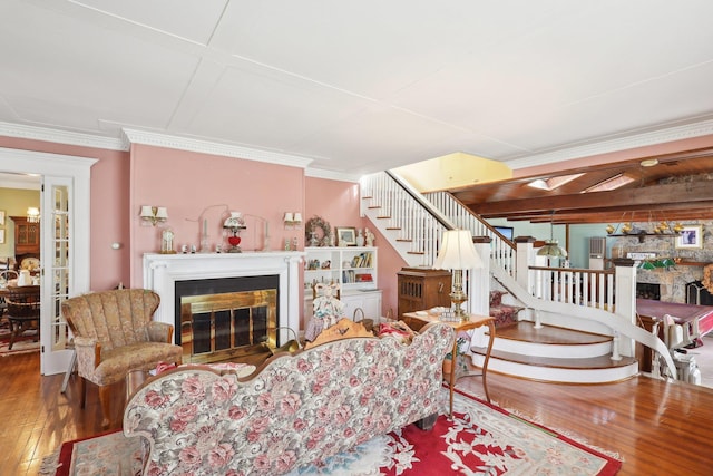 living area featuring a fireplace with flush hearth, ornamental molding, wood-type flooring, and stairs