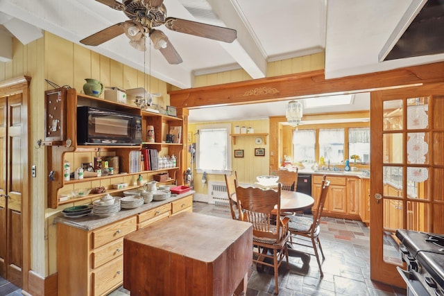 kitchen with wooden walls, ceiling fan, stainless steel gas range oven, beam ceiling, and stone tile flooring