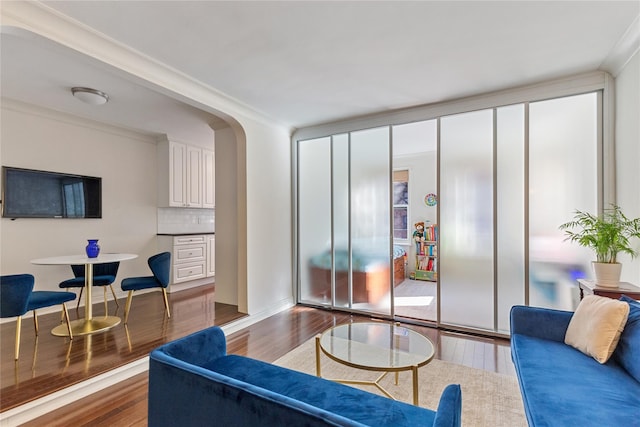 living area with arched walkways, ornamental molding, and wood finished floors