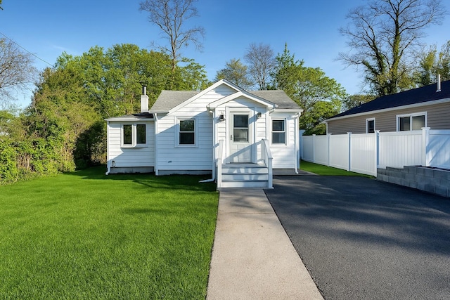 bungalow with fence, a chimney, a shingled roof, and a front lawn
