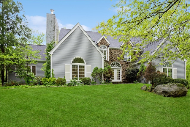 rear view of house with french doors, a lawn, a chimney, and stone siding