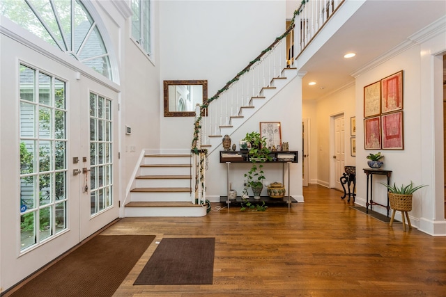 foyer entrance with stairs, wood finished floors, crown molding, baseboards, and a towering ceiling