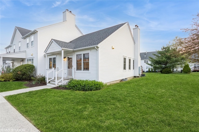 view of front of home with a front lawn, roof with shingles, and a chimney