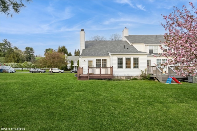 back of property with a lawn, roof with shingles, a chimney, and a deck