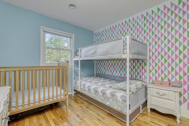 bedroom with wallpapered walls, baseboards, wood finished floors, and an accent wall