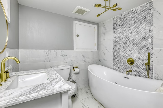 bathroom with tile walls, marble finish floors, toilet, a freestanding bath, and vanity