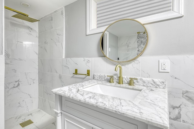 bathroom with tiled shower, vanity, and marble look tiles