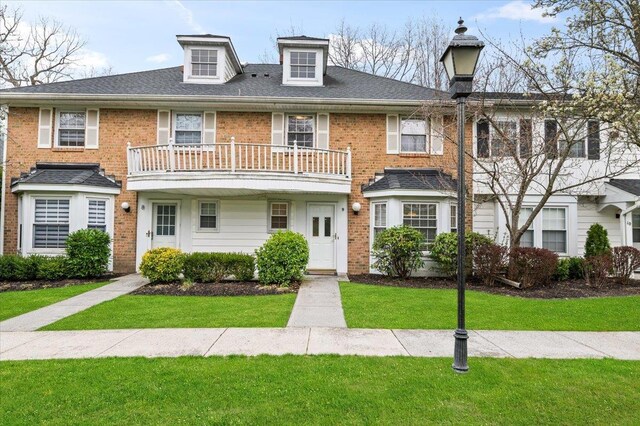 townhome / multi-family property with brick siding, a balcony, and a front yard