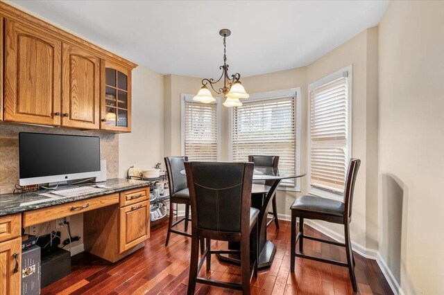 dining area featuring built in study area, baseboards, dark wood-type flooring, and a chandelier