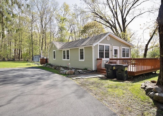 single story home with roof with shingles, a storage unit, a front lawn, a wooden deck, and an outbuilding