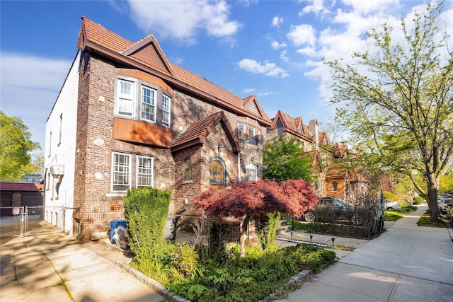 tudor-style house with fence, driveway, and brick siding