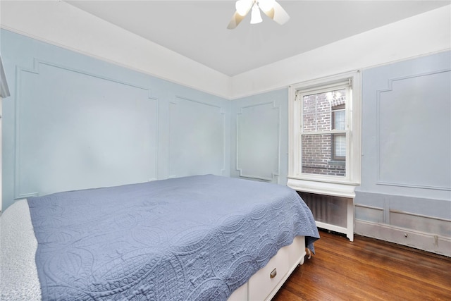 bedroom with radiator heating unit, ceiling fan, wood finished floors, and a decorative wall