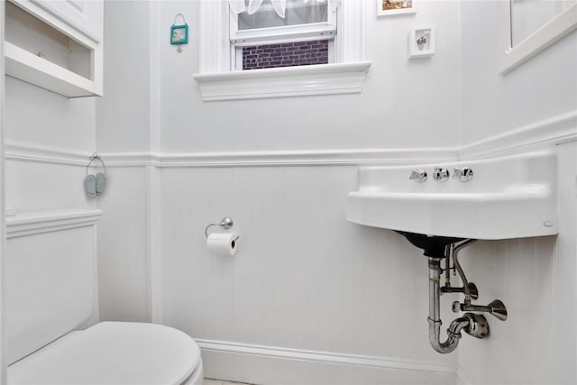 bathroom with toilet, wainscoting, and a decorative wall