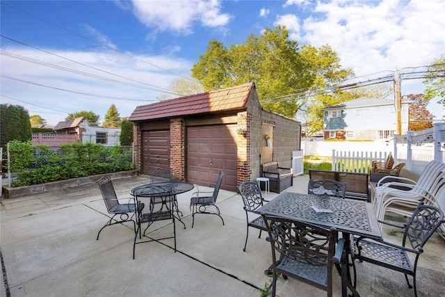 view of patio featuring a garage, fence, an outbuilding, and outdoor dining space