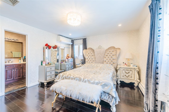 bedroom with wood finish floors, baseboards, a wall unit AC, ensuite bathroom, and visible vents