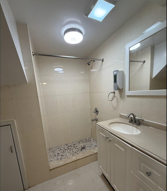 full bath with vanity, tile patterned floors, a tile shower, and tile walls