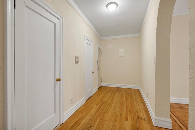 hallway featuring crown molding, light wood-style flooring, a textured wall, and baseboards