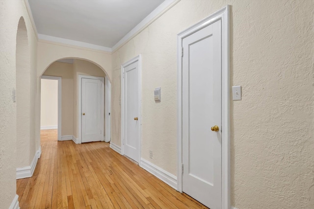 corridor with arched walkways, a textured wall, light wood finished floors, and ornamental molding
