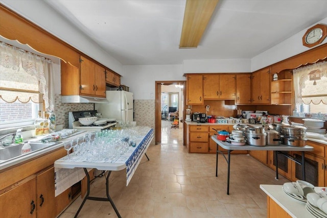 kitchen featuring a sink, freestanding refrigerator, brown cabinetry, stove, and light countertops