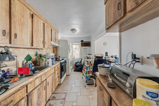 kitchen with a sink, stone tile floors, under cabinet range hood, light countertops, and gas stove