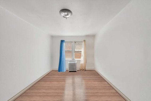 spare room featuring light wood-style floors, baseboards, and radiator heating unit