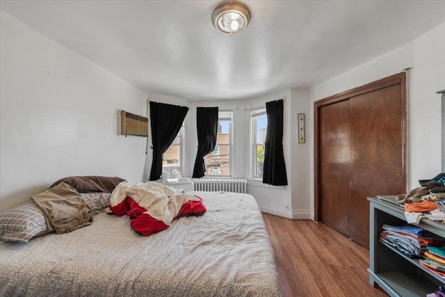 bedroom with baseboards, radiator heating unit, a closet, and wood finished floors