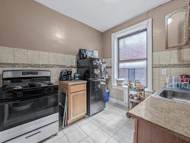 kitchen featuring freestanding refrigerator, tile walls, stainless steel range with gas cooktop, a sink, and light tile patterned floors