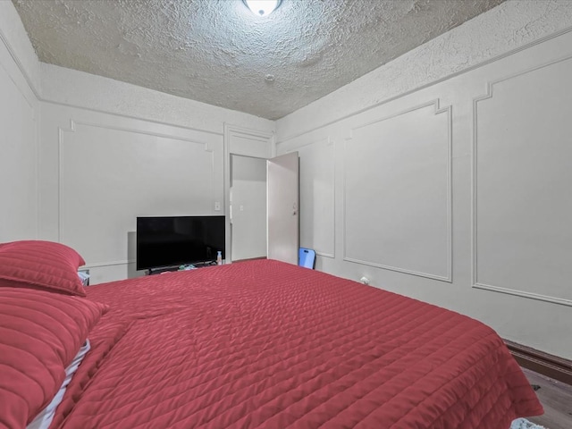 bedroom featuring a textured ceiling, wood finished floors, and a decorative wall