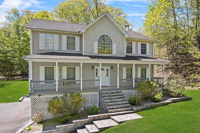 colonial home with roof with shingles, covered porch, a chimney, and a front lawn