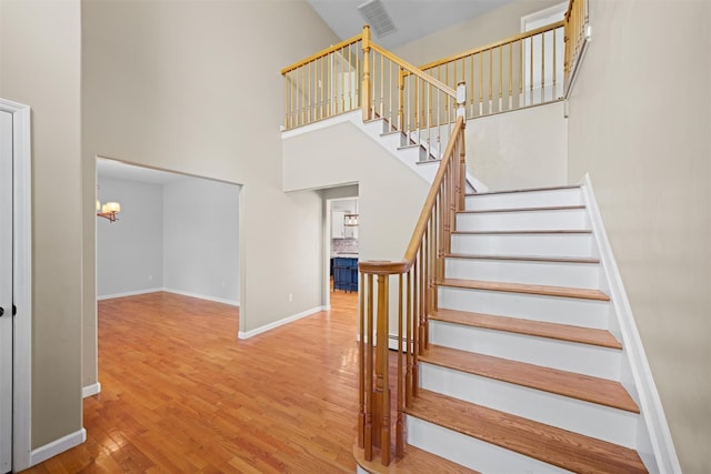 staircase featuring visible vents, an inviting chandelier, wood finished floors, baseboards, and a high ceiling