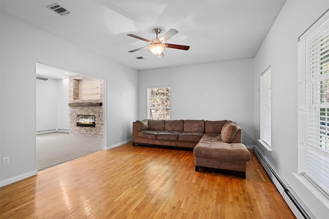 living room featuring a fireplace, visible vents, light wood-style flooring, and a baseboard radiator