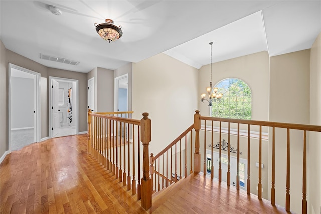 hall with visible vents, wood finished floors, baseboards, an upstairs landing, and an inviting chandelier