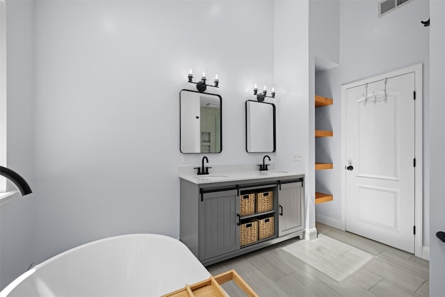 bathroom featuring double vanity, visible vents, wood finished floors, a sink, and a soaking tub