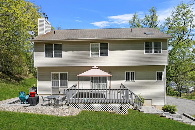 rear view of house featuring a lawn, a wooden deck, a chimney, and a patio area