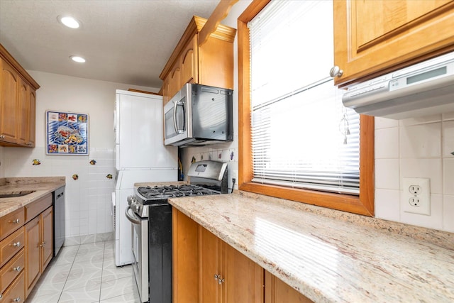 kitchen featuring brown cabinets, light stone countertops, stainless steel appliances, recessed lighting, and tile walls