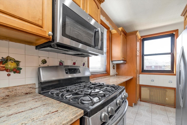 kitchen featuring appliances with stainless steel finishes, tasteful backsplash, and light stone counters