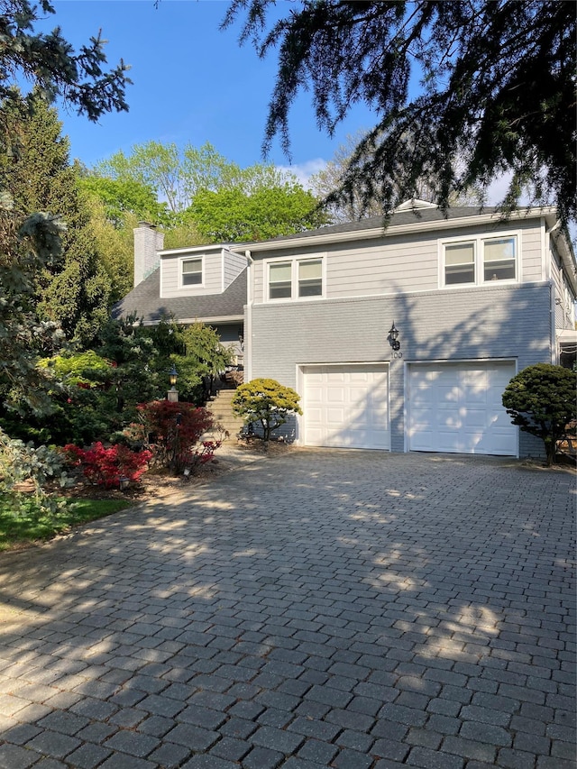 view of front of home featuring brick siding, decorative driveway, an attached garage, and a chimney