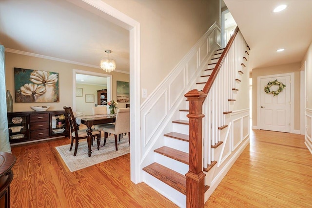 stairway featuring a notable chandelier, ornamental molding, and wood finished floors