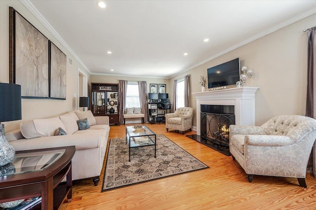 living room with recessed lighting, ornamental molding, wood finished floors, and a lit fireplace