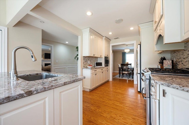 kitchen with visible vents, a sink, light wood finished floors, appliances with stainless steel finishes, and backsplash