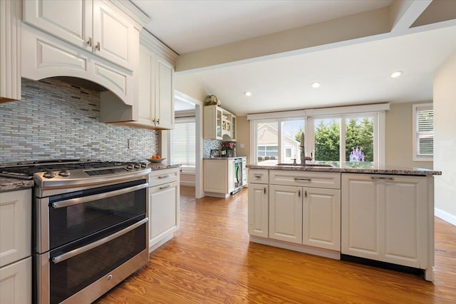 kitchen featuring white cabinets, a sink, light wood-style flooring, double oven range, and backsplash