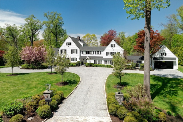 shingle-style home with curved driveway, a front lawn, a chimney, and a garage